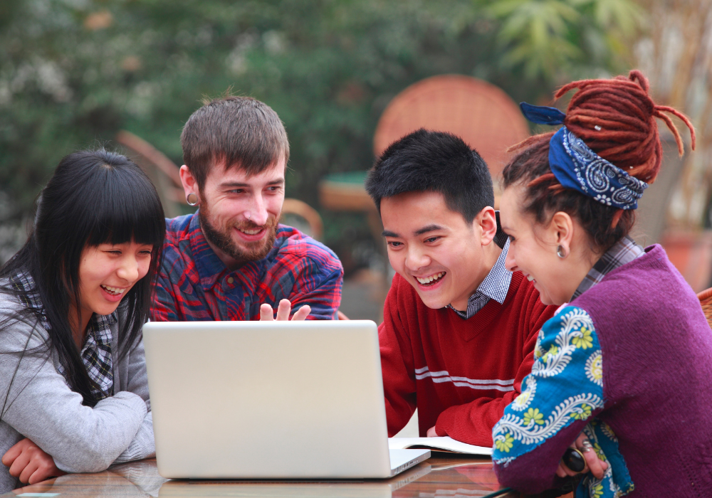 students-outside-facetime-gallery Group of students at a picnic table looking at laptop screen