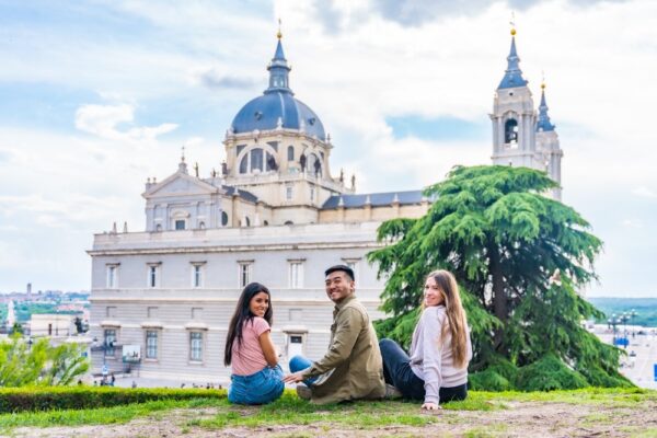 Spain support image 17 Three individuals seated on the grass, enjoying the view of a majestic cathedral.