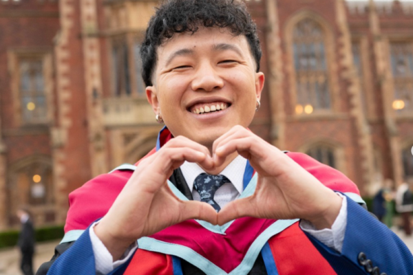qub-overview-2 A young man in a graduation gown forming a heart shape with his hands.